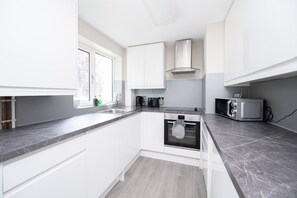 A modern kitchen with white cabinets, a built-in oven, a microwave, and a window providing natural light. - 2 Bed Flat Free Parking Next To The Station (West Sussex)
