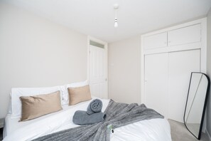 A bedroom with a bed, pillows, a blanket, a door, and a mirror. - 2 Bed Flat Free Parking Next To The Station (West Sussex)