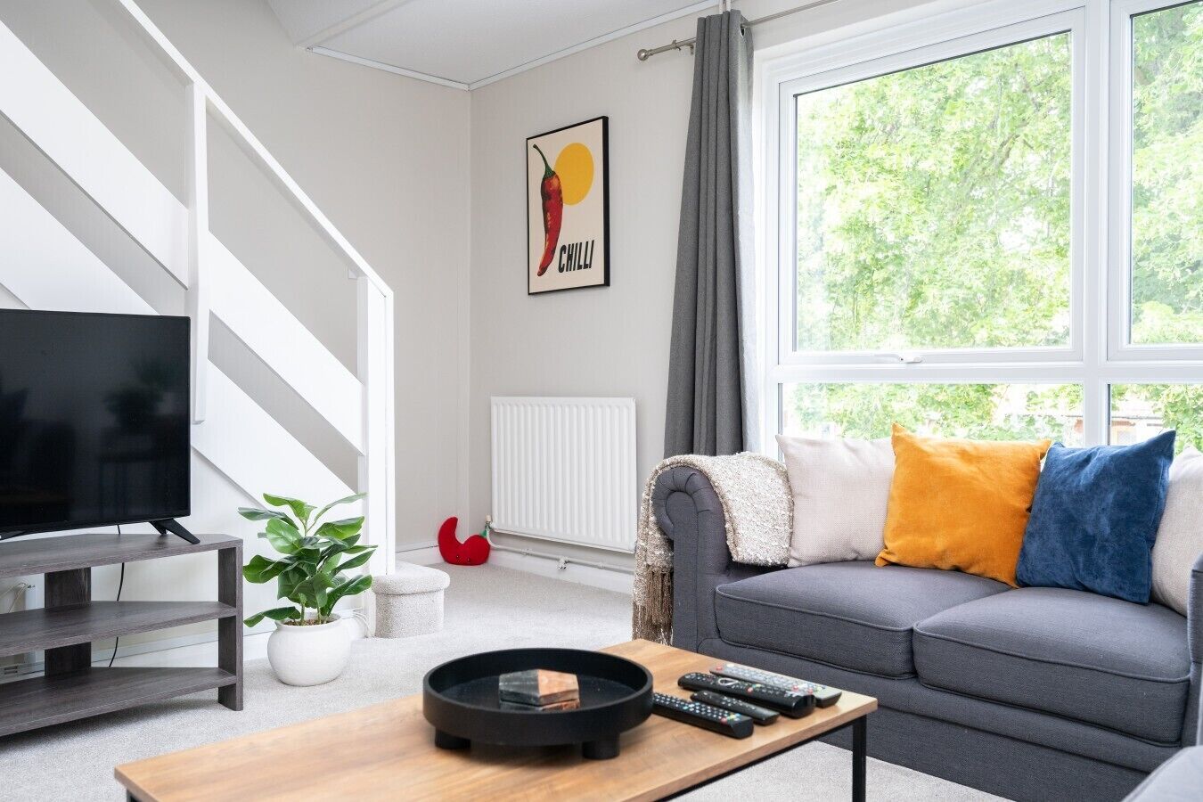 A modern living room with a grey sofa, a flat-screen TV, a coffee table, and a plant.