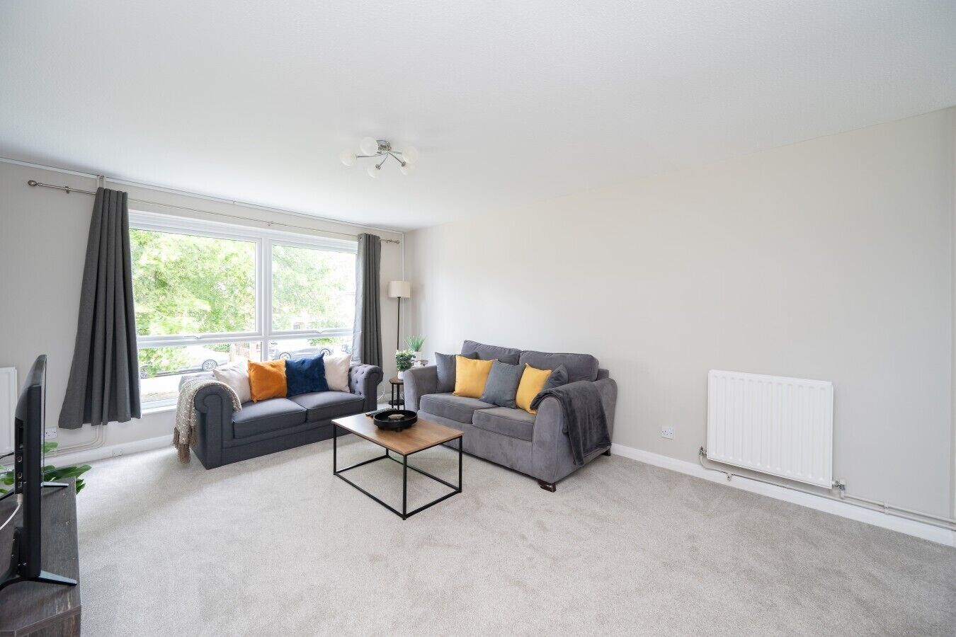 A modern living room with two grey sofas, a coffee table, and a large window with curtains.