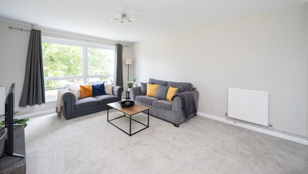 A modern living room with two grey sofas, a coffee table, and a large window with curtains. - 2 Bed Flat Free Parking Next To The Station (West Sussex)