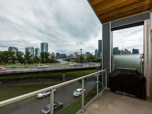 A balcony with a city view, a covered outdoor seating area, and a glass door. - Modern Loft Haven | BBQ, Sleeps 6 | (Calgary)