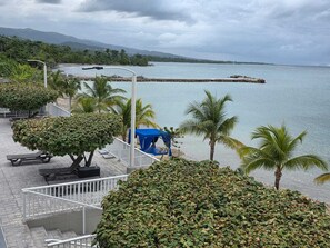 A seaside promenade with a view of the ocean, a blue canopy, and palm trees. - 2 Bedroom Villa, Private Beach, Communal Pool & Gym (Saint Ann's Bay)