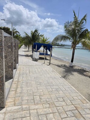 Una passeggiata sulla spiaggia con un'area salotto coperta, palme e vista sull'oceano.