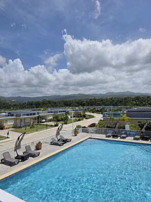 A swimming pool with lounge chairs, a view of a resort area, and distant mountains. - 2 Bedroom Villa, Private Beach, Communal Pool & Gym (Saint Ann's Bay)