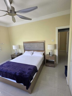 Una camera d'albergo con un letto, due comodini, una ventola a soffitto e una porta che dà su un'altra stanza.