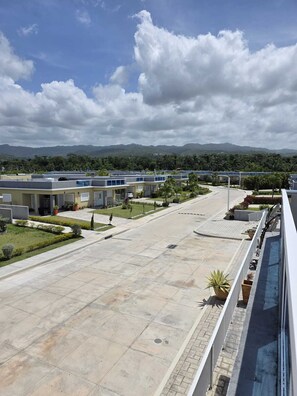 A hotel courtyard with a paved walkway, a pool area, and a view of distant mountains. - 2 Bedroom Villa, Private Beach, Communal Pool & Gym (Saint Ann's Bay)