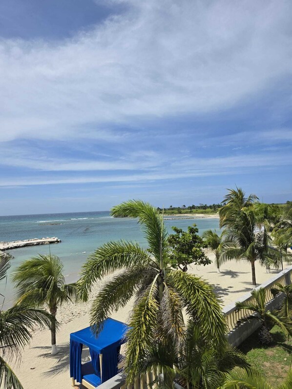 A beach view with palm trees, a blue tent, and a clear sky. - 2 Bedroom Villa, Private Beach, Communal Pool & Gym (Saint Ann's Bay)