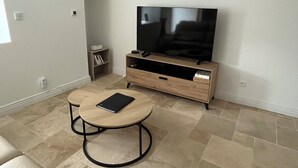 A living room with a TV on a wooden stand, a round table with a book, and a small bookshelf. - Farm cottage (Le Haut-Corlay)