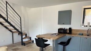 A modern kitchen with a wooden countertop, two black bar stools, a microwave, and a coffee machine. - Farm cottage (Le Haut-Corlay)