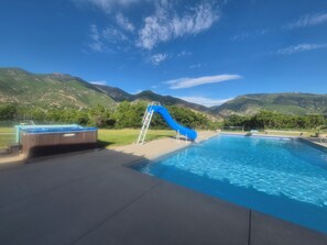 Una piscina con tobogán azul, un jacuzzi y vistas a las montañas.