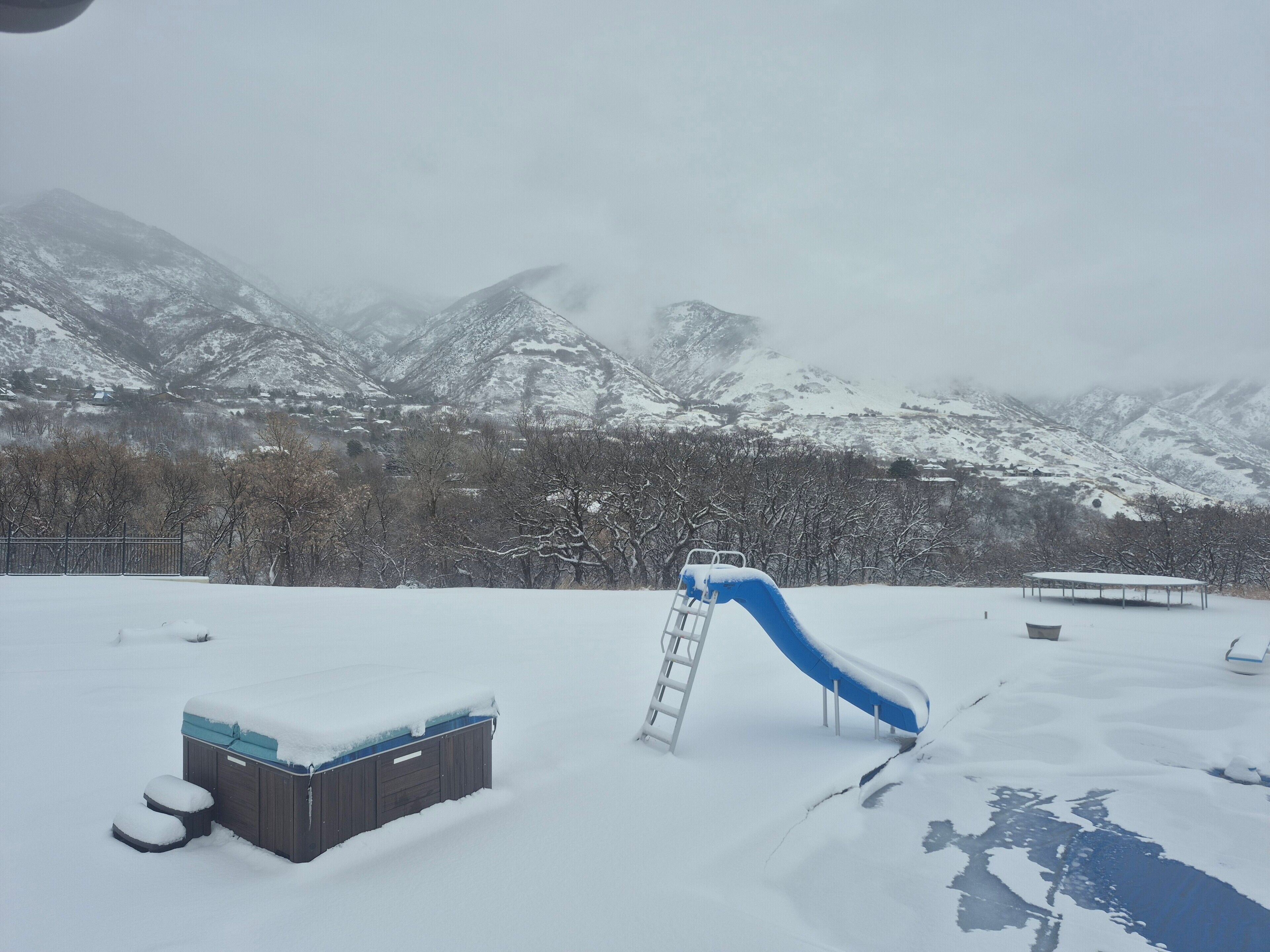 A snowy outdoor area with a slide, a hot tub, and mountains in the background.