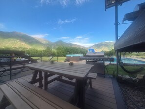 Una terraza con mesas de picnic, una parrilla y una piscina.