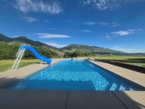 A swimming pool with a blue slide, surrounded by mountains and clear skies.