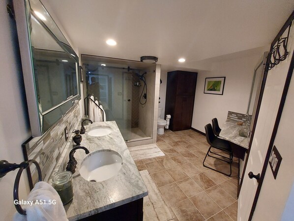 Une salle de bain avec un grand miroir, deux lavabos, une douche et des toilettes.