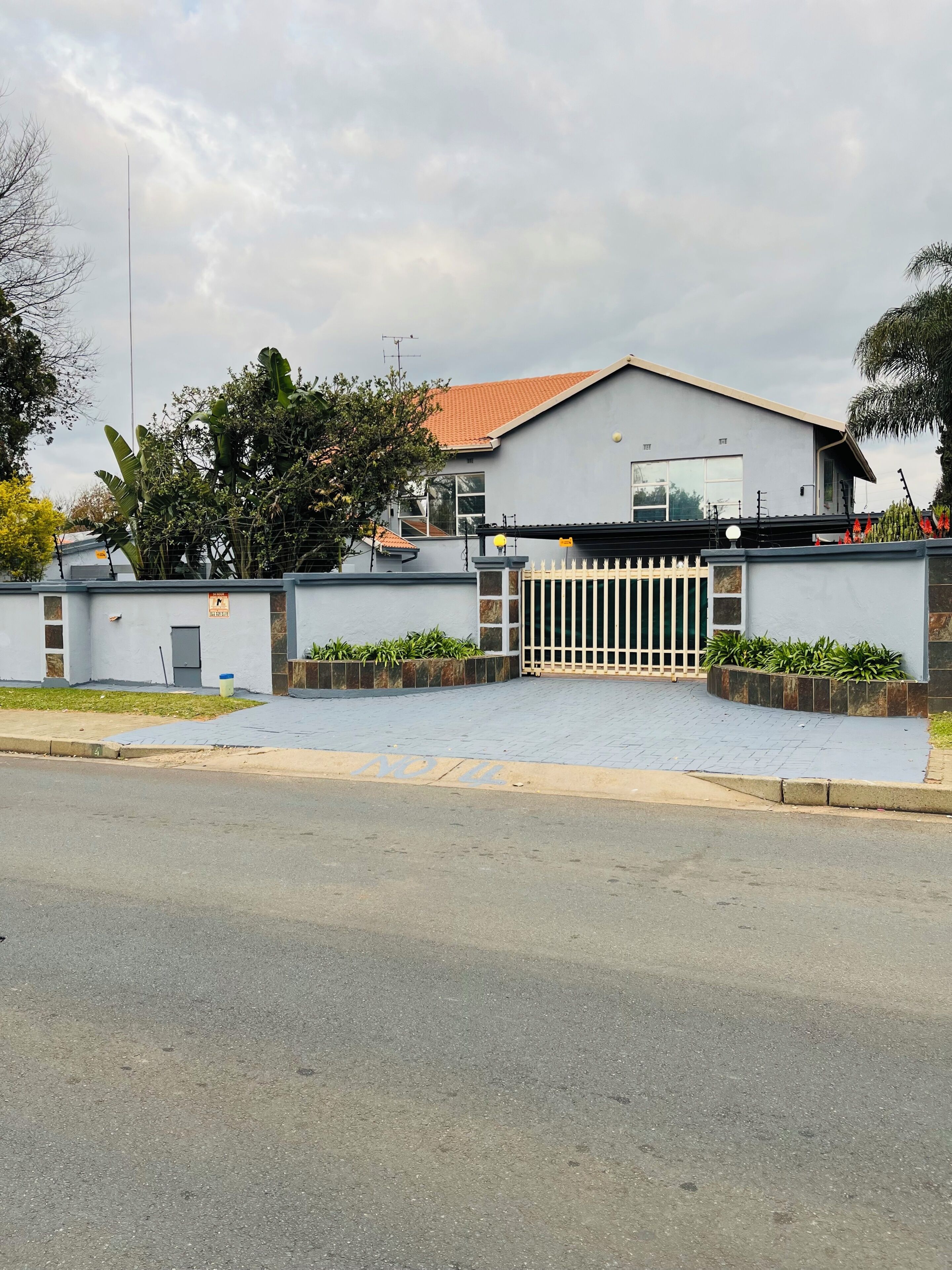A modern two-story house with a gated entrance, a paved driveway, and a well-maintained garden.