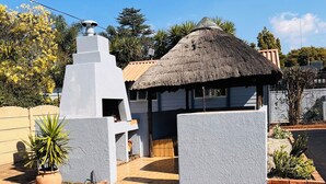 A building with a thatched roof, a white exterior, and a paved entrance area with a potted plant. - Airport Continental Guest House (Kempton Park)
