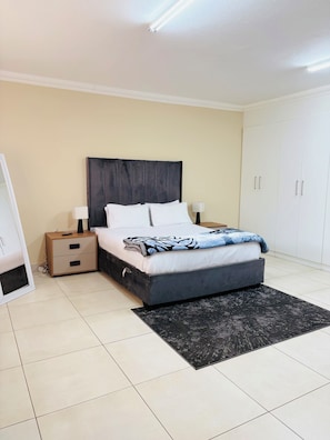 Un dormitorio con cama, mesitas de noche, armario y lámpara de pie.
