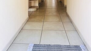 A hallway with a built-in wooden shelving unit, a tiled floor, and a door leading to another room. - Airport Continental Guest House (Kempton Park)