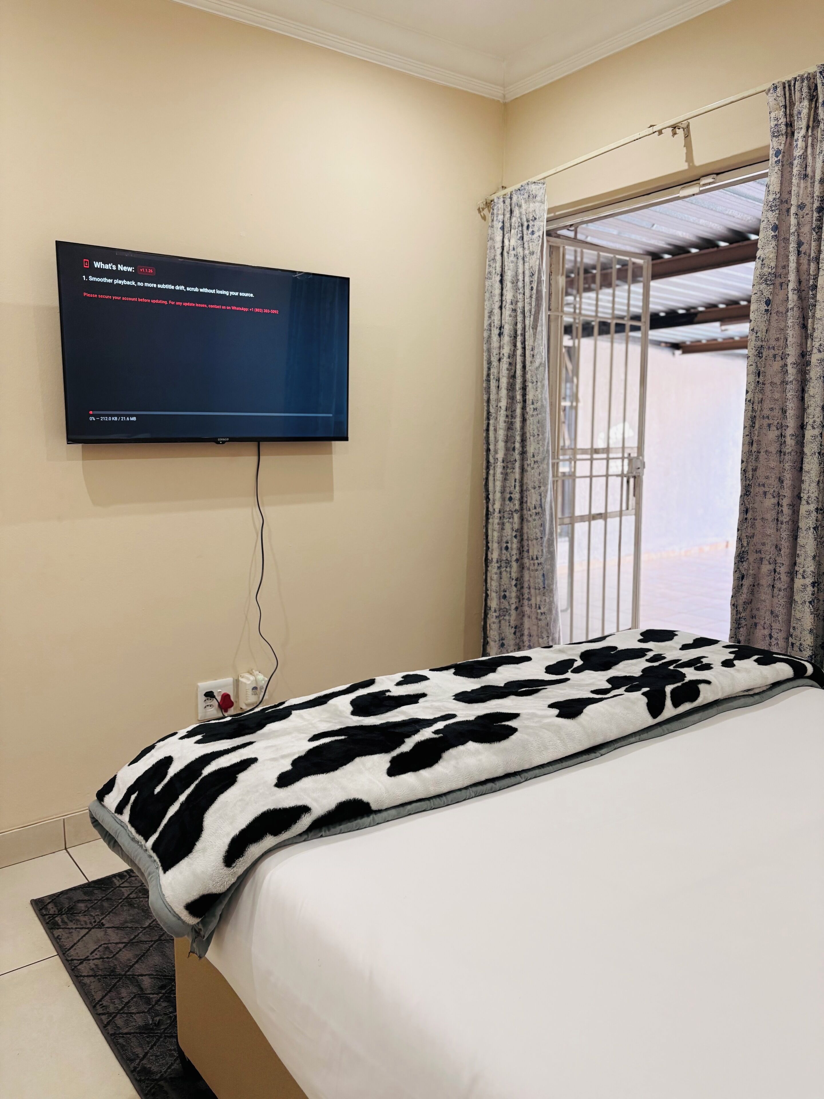 A bedroom with a bed, a television mounted on the wall, and a window with curtains.