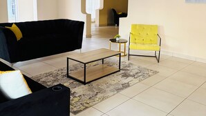 A living room with a black sofa, a yellow armchair, a coffee table, and a painting on the wall. - Airport Continental Guest House (Kempton Park)