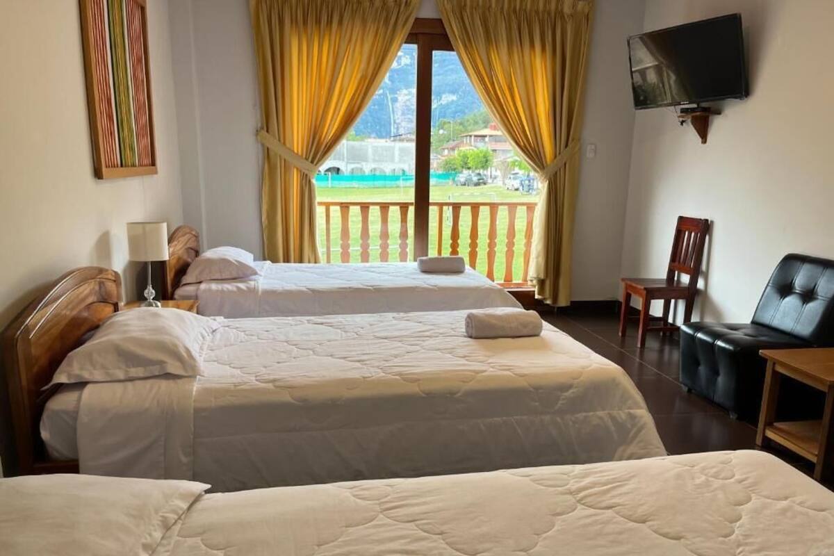 Habitación de hotel con dos camas, televisión, balcón con cortinas amarillas y vistas al exterior.