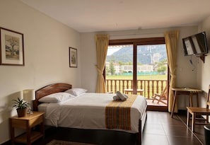 Une chambre à coucher avec un lit, une table de chevet avec une lampe et une plante, un téléviseur et un balcon avec des chaises.