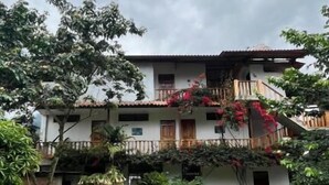 Un edificio de dos pisos con una puerta roja, un balcón y un jardín delantero.