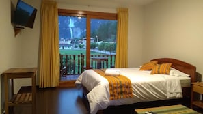 Une chambre dâhĂŽtel avec un lit, une tĂ©lĂ©vision, un balcon avec des rideaux et une vue sur une cascade.