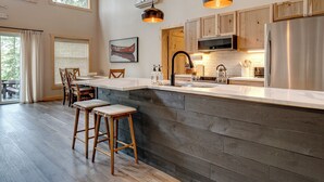 A modern kitchen with a large island, wooden cabinets, and pendant lighting. - NEW Luxury Riverfront Home, large deck, river tubing, kayaks, 5 min to Downtown (Hayward)