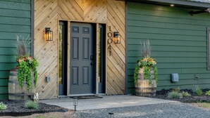 A wooden door with a number plaque, two lantern-style lights, and two planters with plants. - NEW Luxury Riverfront Home, large deck, river tubing, kayaks, 5 min to Downtown (Hayward)