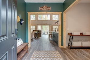 A hallway leading to a dining area with a bench, a rug, and a sign above the door.