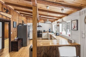 Une cuisine moderne avec des poutres en bois, des appareils électroménagers en acier inoxydable et des luminaires suspendus.