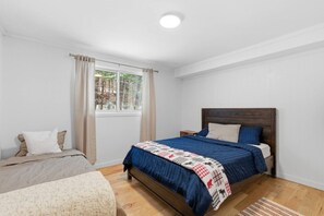 A bedroom with a wooden bed, a window with curtains, a bedside table, and a small rug. - Serene Otter Lake Waterfront | Dock + Fire Pit (Huntsville)