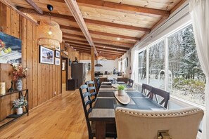 A wooden interior with a dining area, kitchen, and large windows offering a view of a snowy landscape. - Serene Otter Lake Waterfront | Dock + Fire Pit (Huntsville)