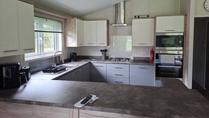 A kitchen with a gas stove, oven, and a window with blinds. - Holiday Lodge with fishing set in tranquil surroundings (Forton)