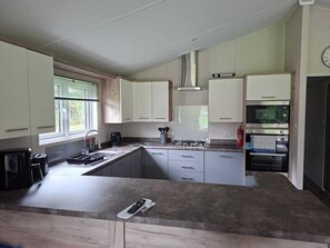 A kitchen with a gas stove, oven, and a window with blinds. - Holiday Lodge with fishing set in tranquil surroundings (Forton)