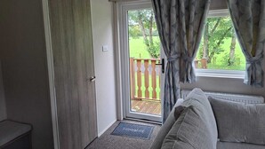 A room with a door leading to a balcony, a window with curtains, and a sofa. - Holiday Lodge with fishing set in tranquil surroundings (Forton)