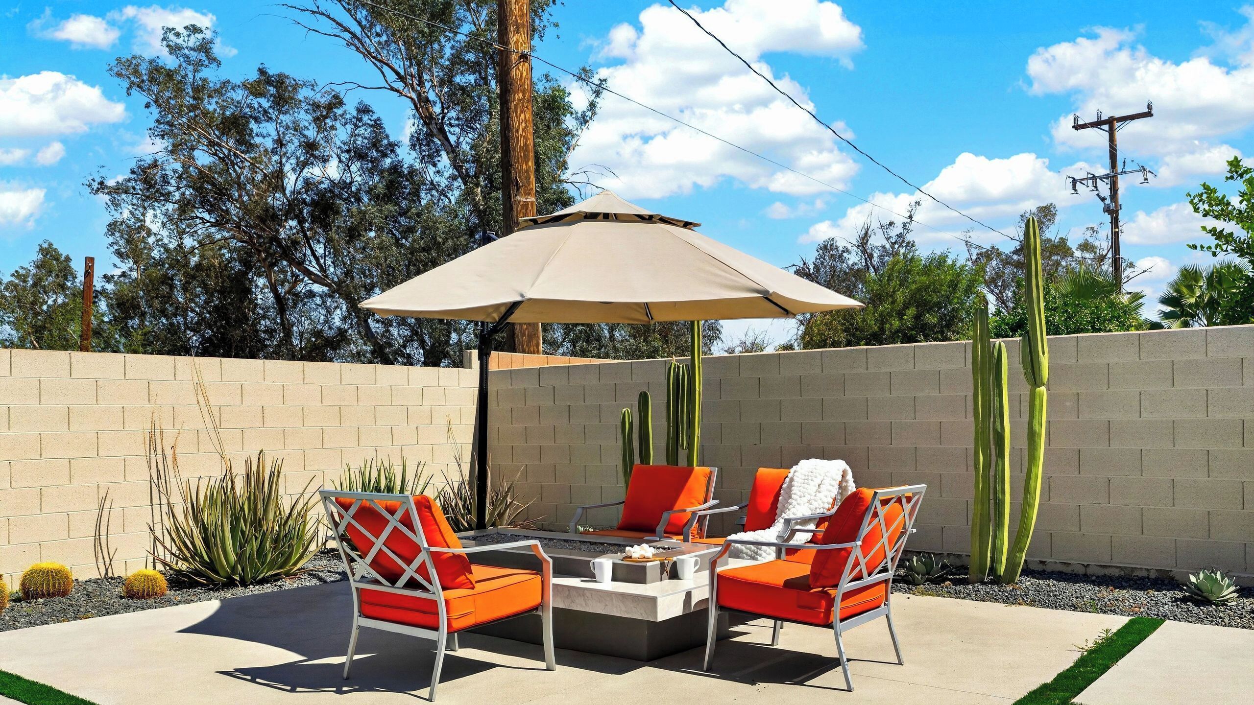 An outdoor patio with a table and chairs, a large umbrella, and cacti.