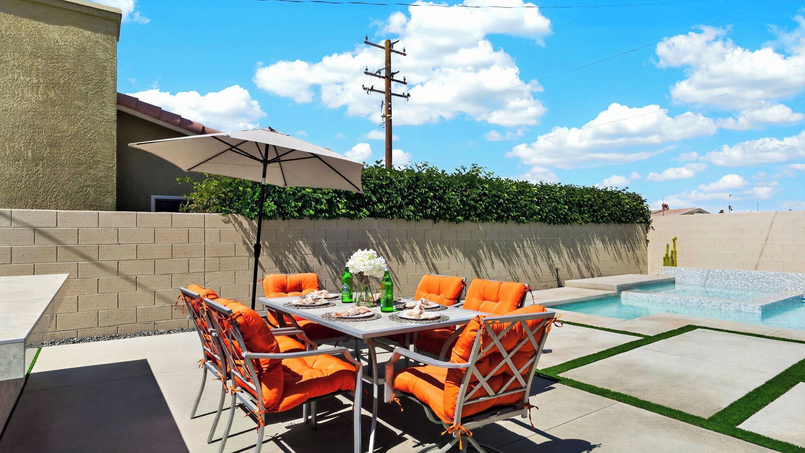 A patio with a table and chairs, a pool, and a hedge.