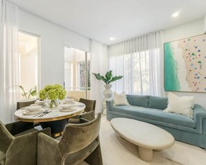 Ein modernes Wohnzimmer mit einem runden Esstisch, einem blauen Sofa und einem großen abstrakten Gemälde.