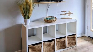 Ein weißer Konsolentisch mit einem darüber angebrachten Flachbildfernseher, einer Topfpflanze und Korbwassern.