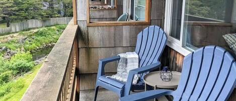 A covered outdoor seating area with two chairs and a small table, overlooking a natural landscape.
