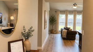 A spacious living area with a wooden floor, a ceiling fan, a large mirror, and a framed welcome sign. - 10 Sleeps, Spacious Family, Friends & Pet Condo, Near Rose Dist & Gathering PL (Broken Arrow)
