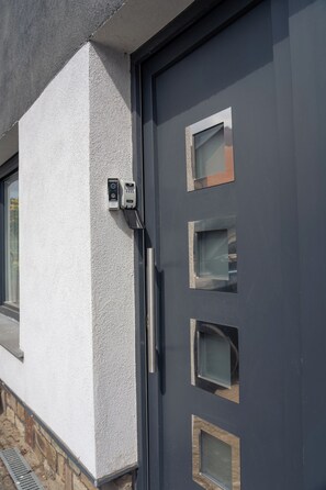 Ein modernes Gebäude mit einer grauen Tür, mehreren rechteckigen Fenstern und einer an der Wand angebrachten Sicherheitsvorrichtung.