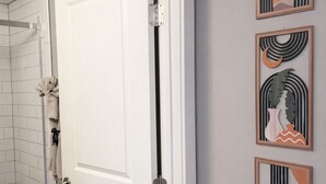 A hallway with a white door, a glass shower enclosure, and three framed artworks on the wall.