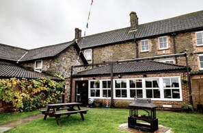A brick building with a tiled roof, a picnic table, and a barbecue grill in the yard.