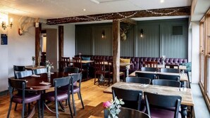 Un interior de restaurante con mesas y sillas de madera, una zona de bar con asientos acolchados y un ciervo decorativo en la pared.