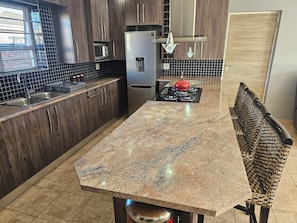 A modern kitchen with wooden cabinets, a stainless steel refrigerator, a microwave, and a gas stove. - Menza Self-catering in George South Africa- Relaxing Home-away-from Home (George)