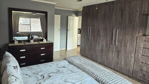 Une chambre à coucher comprenant un lit, une commode, une armoire, un ventilateur de plafond et une vue sur l’extérieur.